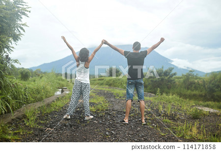 A young, happy couple in love poses in rice fields against the backdrop of Mount Agung volcano on the popular tourist island of Bali. A young, happy couple in love poses in rice fields against the backdrop of Mount Agung volcano on the popular tourist island of Bali. 114171858