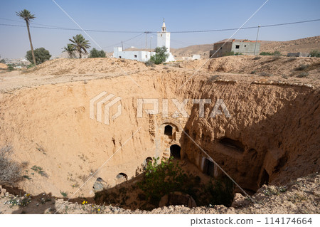 Remnants of cave dwellings in earthen pit and mosque minaret in Matmata Remnants of cave dwellings in earthen pit and mosque minaret in Matmata 114174664