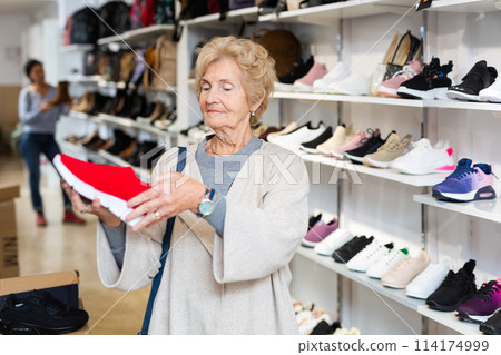 Elderly woman selecting training shoes in shoeshop Elderly woman selecting training shoes in shoeshop 114174999