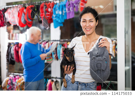 Woman choosing winter clothes for her doberman pinscher dog at pet store Woman choosing winter clothes for her doberman pinscher dog at pet store 114175033