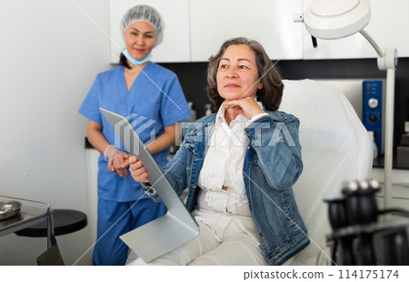 Smiling aged woman looking at mirror after hardware facial procedure 114175174