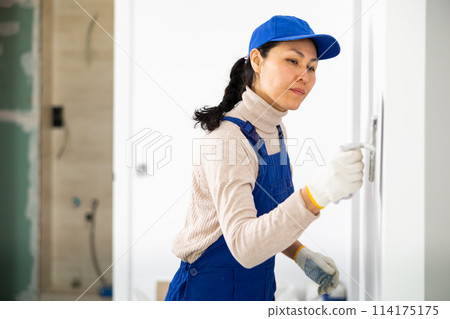 Woman applying plaster to a wall with floated trowel 114175175
