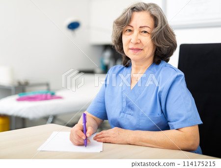 Experienced doctor writes important notes while sitting at workdesk in the cabinet 114175215