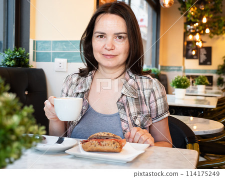 Woman having breakfast in cafe with sandwich and coffee 114175249