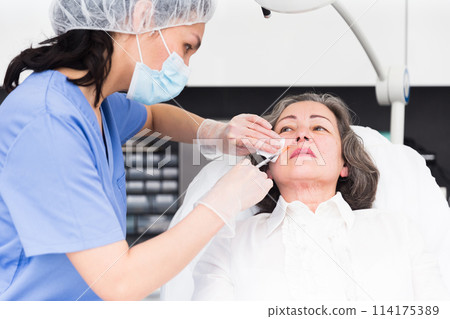 Elderly female client during procedure of face mesotherapy Elderly female client during procedure of face mesotherapy 114175389