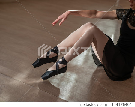 Close-up of the legs of a ballerina sitting on the floor.  114176404