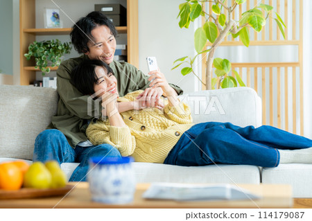 Couple relaxing in the living room looking at their smartphones Couple relaxing in the living room looking at their smartphones 114179087