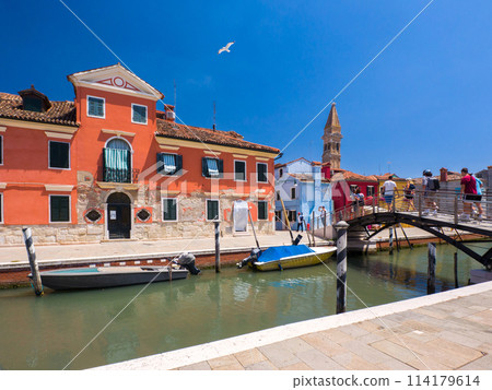 A town with colorful buildings along a waterway with spires in the distance (Burano, Italy) 114179614