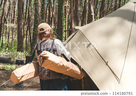 A female camper carries a cot table and sets up a tent at a campsite 114180791