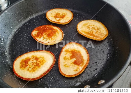 Four Golden Brown Pancakes Cooking on Black Non-stick Pan 114181233