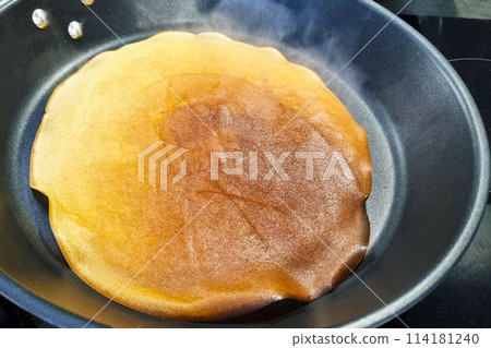 Large Golden Pancake Cooking on Black Non-Stick Frying Pan Large Golden Pancake Cooking on Black Non-Stick Frying Pan 114181240