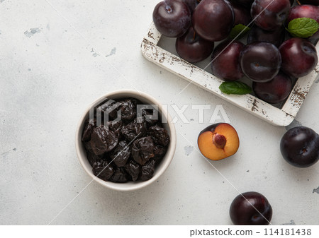 Sweet prunes in glass bowl with ripe plums in wooden box on light kitchen background. Sweet prunes in glass bowl with ripe plums in wooden box on light kitchen background. 114181438