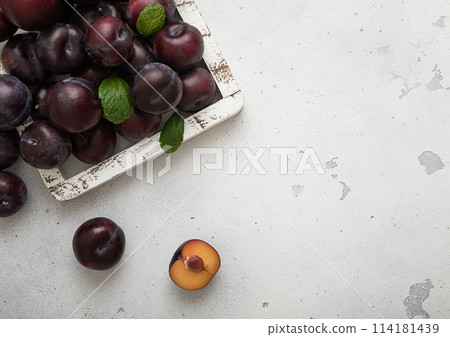 Wooden box of raw ripe purple plums on light kitchen background. Wooden box of raw ripe purple plums on light kitchen background. 114181439