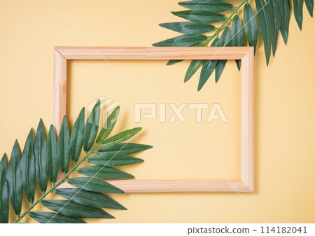 Two palm tree leaf and wooden frame on yellow background. Top view 114182041