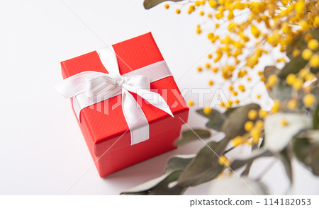 red gift box with white ribbon on white table under spring mimosa flowers 114182053
