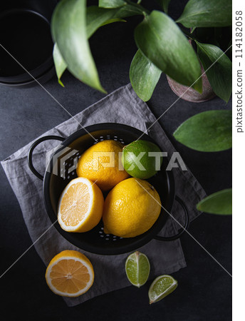 juicy lemons and limes in a black bowl on a gray table. Dark and mood concept juicy lemons and limes in a black bowl on a gray table. Dark and mood concept 114182058