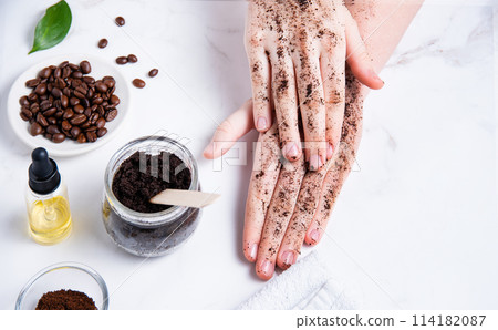 Spa concept. A young woman does a hand massage with a homemade coffee scrub with olive oil Spa concept. A young woman does a hand massage with a homemade coffee scrub with olive oil 114182087