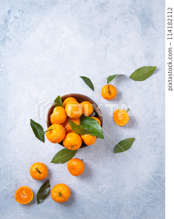 Flat lay sweet and juicy tangerines in a wooden bowl and a few tangerines on a blue background Flat lay sweet and juicy tangerines in a wooden bowl and a few tangerines on a blue background 114182112