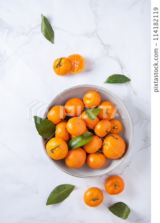 sweet and juicy tangerines in a ceramic  bowl  on a white marble background. 114182119