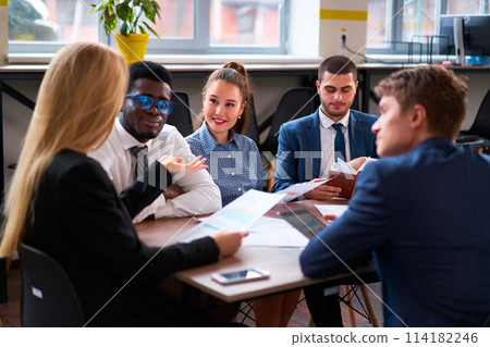 Multiethnic business team engages in a collaborative meeting at modern office. African, Asian, Caucasian colleagues analyze data, discuss strategies. Smartly dressed men, women focus on work progress. Multiethnic business team engages in a collaborative meeting at modern office. African, Asian, Caucasian colleagues analyze data, discuss strategies. Smartly dressed men, women focus on work progress. 114182246