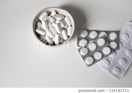 White pills in bowl and blister tablets on white background 114182713