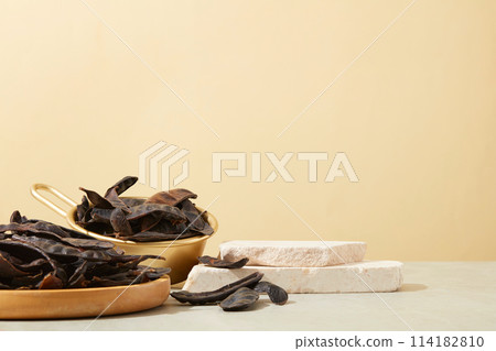 A stack of stone podiums displayed with a wooden dish and a golden bowl containing many black locust. Minimal podium display for cosmetic product presentation A stack of stone podiums displayed with a wooden dish and a golden bowl containing many black locust. Minimal podium display for cosmetic product presentation 114182810