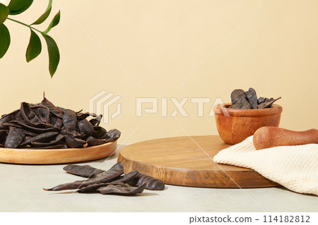 Cutting board with a mortar containing black locust and a pestle placed on with a scarf. Many black locust displayed on a dish. Empty space for natural product advertising  114182812