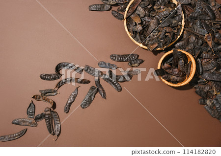 Minimal scene of many black locust fruits scattered on brown surface. Two bamboo baskets of black locust featured. Black Locust (Fructus Gleditschiae) is mainly used in beautifying hair Minimal scene of many black locust fruits scattered on brown surface. Two bamboo baskets of black locust featured. Black Locust (Fructus Gleditschiae) is mainly used in beautifying hair 114182820