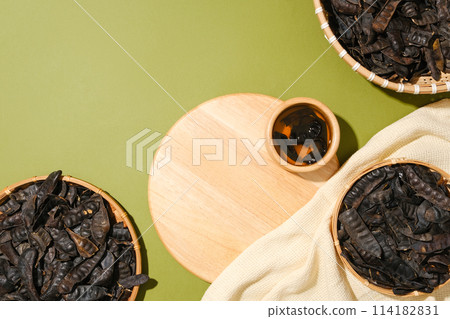 Wooden cutting board with a bowl of liquid displayed on. Few bamboo baskets of black locust fruits arranged around. Products with Black Locust extract can be showed on blank space 114182831