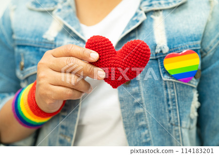 Asian lady wearing rainbow flag wristbands and hold red heart, symbol of LGBT pride month celebrate annual in June social of gay, lesbian, bisexual, transgender, human rights. 114183201