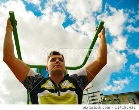 Man flexing arms in outdoor gym Man flexing arms in outdoor gym 114183432
