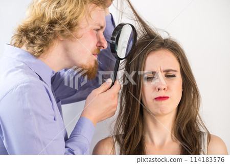 Man looking at woman hair through magnifer Man looking at woman hair through magnifer 114183576