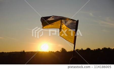 Young man in military uniform waving flag of Ukraine against beautiful sunset at background. Male ukrainian army soldier lifted national banner at countryside. Victory against russian aggression 114186005