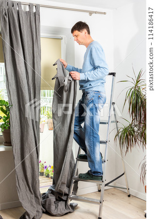 A man hangs curtains 114186417