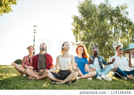 Group of adult mix-race friends meditating while practice yoga outside in park. Group of adult mix-race friends meditating while practice yoga outside in park. 114186848