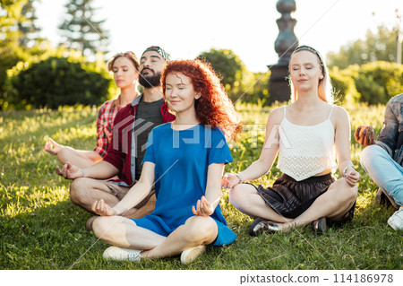 Group of adult friends meditating while practicing yoga outside in park. 114186978