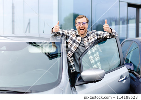Great Car. Cheerful guy standing near auto, gesturing thumbs up buying vehicle in dealership center 114188528