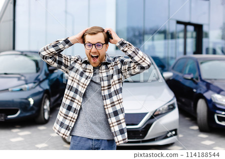 A young man is very impressive and happy, standing in front of his new car A young man is very impressive and happy, standing in front of his new car 114188544