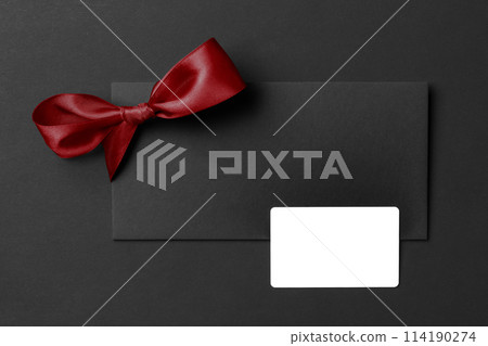 Mockup of white gift card on greeting card with red bow at black paper. 114190274