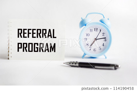 Notepad with the inscription REFERRAL PROGRAM on a white background with a clock and a pen. t. 114190458