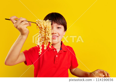 Smiling Korean boy, child in red polo shirt lifting noodles with fork against yellow background. Fast instant food dinner 114190656