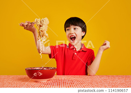 Cheerful emotional child playfully lifting noodles with fork against yellow background. Playful eating 114190657