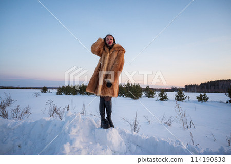 A beautiful girl in a fur coat walks and has fun in the winter forest 114190838