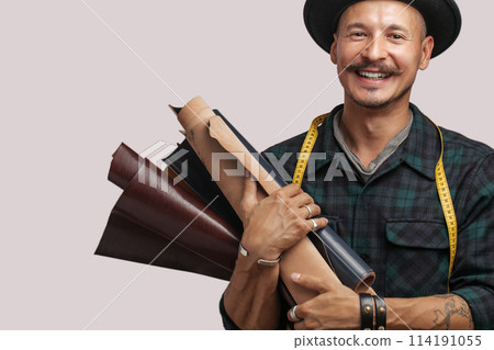 Artisan of leather in creative black hat posing with leather goods in studio. Artisan of leather in creative black hat posing with leather goods in studio. 114191055