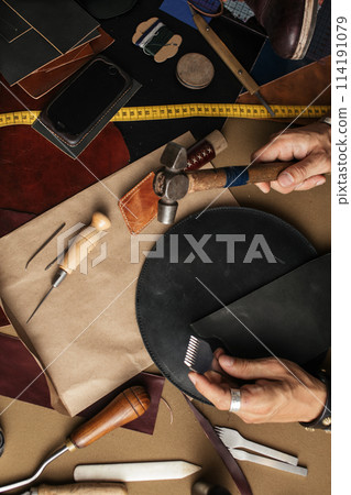 Close up of skinner craftsman working with natural leather using craft tools. 114191079