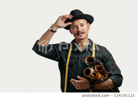 Artisan of leather in creative black hat posing with leather goods in studio. Artisan of leather in creative black hat posing with leather goods in studio. 114191115