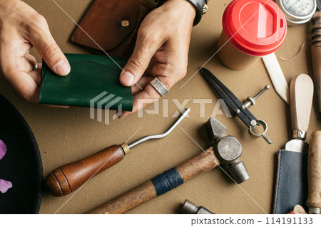 Leather goods master and handmade leather wallets. Workflow in the workshop. Leather goods master and handmade leather wallets. Workflow in the workshop. 114191133
