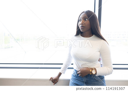 Confident Young Black Woman Posing by Window with Urban Background 114191307