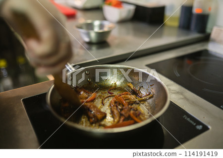 Cook in gloves stirs frying vegetables with kitchen spatula Cook in gloves stirs frying vegetables with kitchen spatula 114191419