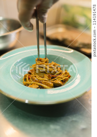 Chef twists noodles around metal chopsticks serving dish 114191478